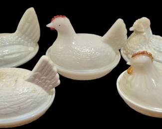 4039 - Milk Glass Hen on Nest Covered Dishes 4"x5" (Description): Collection of three milk glass hen on nest  covered dishes, measuring 4 inches by 5  inches plus two extra lids. The pieces  feature white milk glass construction with  some displaying painted accents including blue and red coloring on the heads and combs.  These decorative covered dishes are classic  examples of traditional milk glass hen  figurines used for candy, eggs, or as  decorative accent pieces. Some chips and