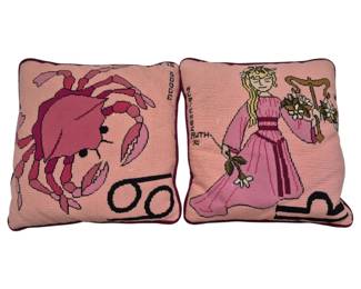 1264 - Pr Needlepoint Zodiac Pillows Cancer & Virgo (Description): Pair of handmade needlepoint pillows  featuring zodiac signs. One pillow depicts  Cancer with a pink crab and the astrological  symbol, the other shows Virgo as a maiden in  a pink gown holding flowers and wheat. Both pillows have pink backgrounds with burgundy  piping trim. Each measures 13" x 13".