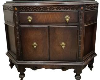 3970 - Carved Depression Era Server 39"x46"x18" (Description): Featuring rich mahogany-toned wood with a  canted front design. The piece showcases  decorative carved scallop detailing along the  top rail and beaded molding accents.  Features one long drawer above a two-door cabinet, all fitted with ornate brass  drop-pull hardware. The server rests on  turned bun feet with a scalloped apron.