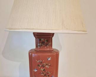 4091 - Chinese Ceramic Table Lamp w/ Floral Motif (Description): Oriental table lamp featuring a square  vase-form body with a coral pink glaze. The  lamp is decorated with hand-painted flowering  prunus branches, birds in flight, and  delicate foliage in a traditional Chinese style. The ceramic base is mounted on a gilt  wood stand with beaded trim detail. Includes  a cream pleated fabric shade. Measures 30  inches tall. Note: lamp requires tightening. Used as is electric/electronic/mechanical