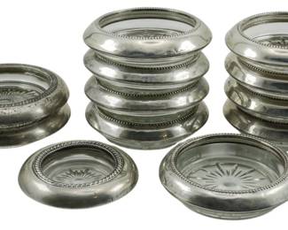 116 - 12 Sterling & Glass Bottle Coasters (Description): A collection of twelve sterling silver and  glass bottle coasters from varying makers.  Each coaster features a sterling silver rim  with a glass insert, displaying various  decorative patterns and beaded edge details.