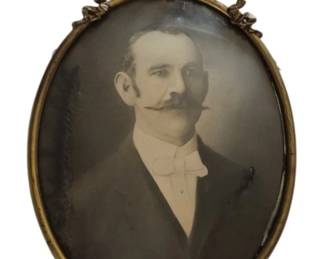 1318 - Antique Oval Bubble Glass Frame 9.25"x5" (Description): Antique oval bubble glass frame featuring a  convex glass front and decorative brass  ribbon bow crest at the top. The frame  contains a Victorian-era sepia-toned  photograph portrait of a gentleman. Measures 16 inches by 11 inches.