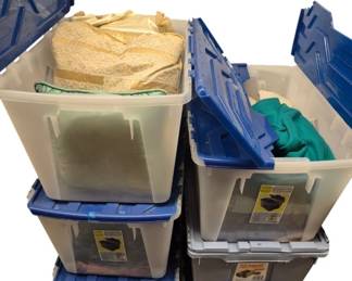 4018 - 4-7 Totes of Linen, Clothes & Fabric (Description): Collection of four to seven plastic storage  totes containing assorted linens, clothing,  and fabric. The totes feature blue lids and  clear bases, with contents visible including  cream-colored lace textiles, green fabric, and various other cloth items. Totes are  included with the lot.