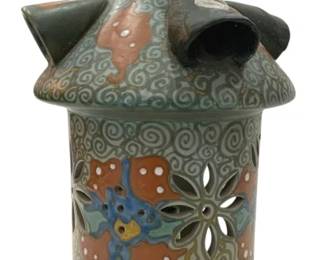 945 - Holland Pottery Candle Holder (Description): A Holland pottery lantern featuring pierced  decorative openwork with floral motifs. The  cylindrical body displays hand-painted  flowers in earth tones of rust, blue, and  green against a gray-green ground with scrollwork patterns. The conical lid features  a loop handle and chimney opening. The base  transitions to a cream color with decorative  blue dash accents along the bottom edge.
