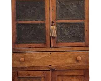509 - Antique Punched Tin Pie Safe 79"x38"x19" (Description): Antique American pine pie safe featuring six  punched tin panels with decorative floral and  star motifs on the upper cabinet doors. The  piece is constructed in two sections with a  single drawer at the waist fitted with wooden knob pulls, and a lower cabinet with two  paneled doors. The case displays  characteristic country or primitive styling  with a molded cornice top and bracket feet.  The warm, honey-toned pine shows beautiful