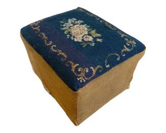 1350 - Needlepoint Stool 8"x12"x10" (Description): A needlepoint stool featuring a floral design  on a dark blue background with decorative  scroll accents. The base is upholstered in a  tan fabric.