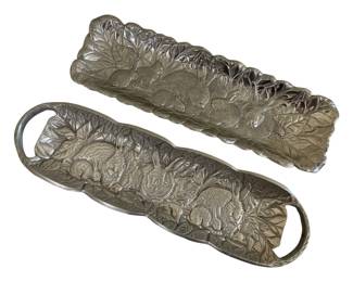 583 - 2 Arthur Court Style Bunny Rabbit Trays (Description): Pair of decorative metal serving trays  featuring embossed bunny rabbit designs amid  detailed foliage. Both trays display a  silvery pewter-like finish with intricate  relief work showing rabbits nestled among leaves and branches. One tray features  integrated loop handles on each end, while  the other has a scalloped leaf-form edge.  Each measures approximately 9 inches by 5  inches.