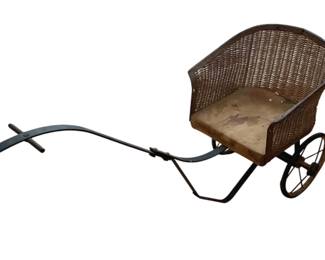 1338 - Antique Child's Wicker Carriage Trike (Description): Antique child's carriage trike featuring a  wicker basket seat mounted on a metal frame  with two wheels and pull handle. This  charming piece combines the style of a  carriage with the functionality of a child's tricycle.