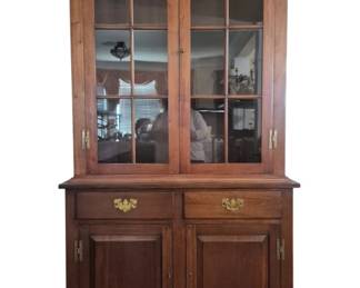 315 - Walnut One-Piece Hutch Cabinet by Howerton (Description): Cherry wood two-piece hutch cabinet featuring  a dentil molding crown, upper section with  two glass-paned doors with six-light  mullions, and brass hinges. The lower section  includes two drawers with brass bail pulls and two panel doors with brass hard
