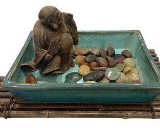 940 - Decorative Buddha in Bowl & Bamboo Tray (Description): Decorative Buddha displayed in a teal glazed  ceramic dish with polished river stones, all  resting on a bamboo tray base. The seated  Buddha figure has a brown finish and  contemplative pose. Measures 17" x 9" x 7".