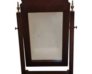 3716 - Howerton Mahogany Cheval Shaving Mirror (Description): Vintage mahogany shaving mirror in the  Chippendale style, featuring a tilting frame  with brass urn finials and side adjustment  knobs. The mirror is mounted on a sturdy  trestle base with splayed feet. The shaped crest displays elegant scrollwork typical of  Georgian-inspired design. Measures 23 inches  high by 12 inches wide by 8 inches deep.