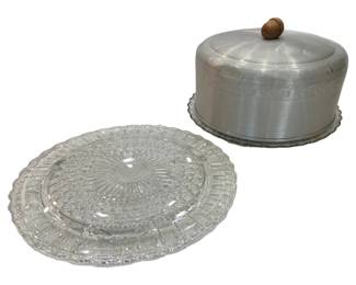 932 - 2 Pressed Glass Cake Plates w/ Aluminum Cover (Description): Featuring an intricate sunburst and bubble  pattern with a scalloped edge, accompanied by  an aluminum dome cover with a wooden knob  finial. The cover displays an embossed  decorative border pattern.