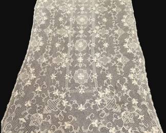 353 - Lace Tablecloth 57.5"x108" (Description): Lace tablecloth featuring an intricate floral  and scrollwork pattern throughout. Measures  57.5 inches by 108 inches.
