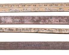 4164 - 4 Wooden Advertisement Yard Sticks (Description): A collection of four wooden advertisement  yard sticks. These vintage measuring tools  feature printed advertising from various  businesses and merchants, serving as both  functional measuring instruments and promotional items from their era.