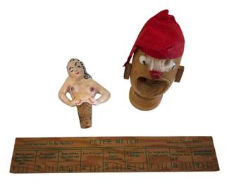 563 - Lot of Vtg Kitsch Novelties Barware Items (Description): A lot of vintage kitsch novelties including a  ceramic nude female figure bottle stopper  with cork base, a carved wooden nutcracker in  the form of a man's head wearing a red cap,  and a wooden "Peter Meter" novelty ruler with humorous measurements and text. These  playful mid-century barware and novelty items  showcase the risque humor popular in their  era.