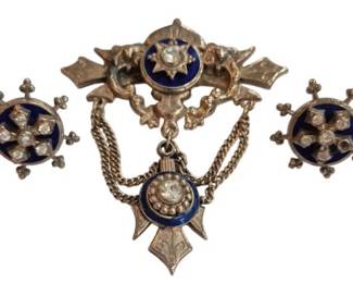 1980 - Victorian Enamel Pin & Earrings Set (Description): A Victorian-style pin and earrings set  featuring enamel accents and clear stone  embellishments. The brooch displays an ornate  bar design with a suspended pendant  connected by delicate chains, while the matching earrings feature a circular  medallion motif with radiating decorative  elements. The gold-tone metalwork exhibits  intricate scrollwork and period detailing  characteristic of Victorian jewelry.