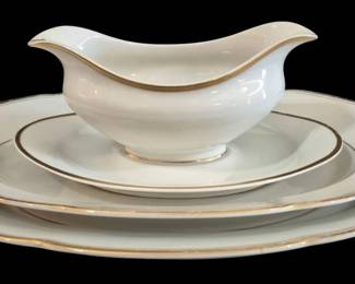 505 - Limoges White Porcelain Platters & Gravy Boat (Description): A set of Lamogi white porcelain serving  pieces featuring two oval platters and a  matching gravy boat. Each piece is elegantly  decorated with gold gilt trim along the  scalloped edges and subtle gold accents. The gravy boat features a graceful elongated form  with gold banding. The set shows classic  European-style design with refined gold  detailing throughout. Measures 15" x 10.5".