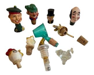 566 - Lot of Decorative Wine Bottle Stoppers (Description): A collection of decorative wine bottle  stoppers featuring a variety of figural  designs. The lot includes several  hand-painted carved wooden character heads  with cork bases, including jovial faces wearing berets and hats. Also included are a  teal glass stopper, a brass pourer with cork,  a ceramic rooster head stopper, a  shell-topped stopper, and clear glass figural  stoppers. An eclectic assortment suitable
