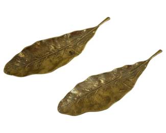 562 - 2 Virginia Metal Crafters Brass Tobacco Leaves (Description): A pair of Virginia Metalcrafters tobacco leaf  trays in cast brass with a warm, aged  patina. Each tray features detailed veining  and naturalistic form, faithfully replicating  a tobacco leaf. These classic decorative trays are ideal for serving, display, or as  catchalls. Measures 9 inches by 2.5 inches.