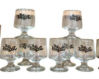 3967 - Vtg Bar Glasses The Tomcat Formula 1 Red (Description): Collection of vintage bar glasses featuring  three distinct designs. Includes stemmed  goblets with "The Tomcat" logo in brown  script, smoky-based cocktail glasses with  "Formula 1" blue and white graphics, and tall champagne flutes marked "Red Rebel" with a  knight logo. The assortment totals  approximately twelve glasses in various sizes  and styles, characteristic of 1970s-1980s  promotional barware.