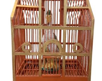 901 - Painted Wood Bird Cage w/ Bird & Stand (Description): Decorative painted wood bird cage with bird  and stand. This charming Victorian-style  birdcage features an architectural design  with a peaked roof topped with finials,  vertical bars in an orange-red hue with cream and gold painted trim accents. The cage  includes a decorative bird figure inside. The  piece rests on an ornate carved dark wood  stand with pierced scrollwork and curved  feet. Measures 16" x 43" x 14".