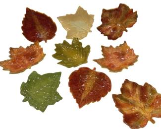 1231 - Ceramic Autumn Leaf Shaped Dishes Set of 9 (Description): A collection of nine ceramic dishes shaped as  autumn leaves. The set features various leaf  forms including maple and aspen in seasonal  fall colors of deep reds, oranges, greens,  and cream. Each dish has molded vein detailing and a glossy glaze finish, suitable  for use as decorative accent pieces or small  serving dishes.