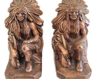 428 - Indian Bookends Copper Overlay 9"x4" (Description): Pair of decorative bookends featuring  kneeling Native American figures in  traditional headdress, finished with copper  overlay. The figures are depicted in a  contemplative pose with detailed feathered headdresses flowing down their backs. Each  bookend measures 9 inches by 4 inches.