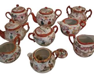 3999 - Group of Satsuma Creamers & Teapots (Description): A group of Satsuma creamers and teapots  featuring traditional Japanese hand-painted  decoration. The collection includes multiple  teapots with lids, sugar bowls, and creamers,  all decorated with figural scenes depicting geishas and landscapes within cartouche  panels. Each piece features characteristic  rust-red accents on handles, spouts, and rims  with delicate floral and scenic motifs on a  white ground.