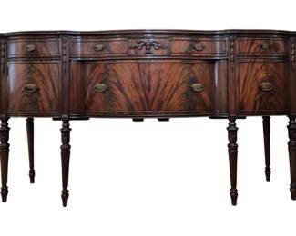 302 - Antique Flame Mahogany Sheraton Style Buffet (Description): 38.5 x 68 x 21.5 Antique flame mahogany buffet in the Sheraton  style, featuring a serpentine front with  elegant book-matched veneer panels. The piece  includes multiple drawers and cabinet doors with brass bail pulls, decorative carved  accents on the center drawer, an