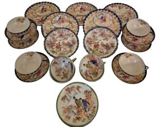 4001 - Blue & Green Satsuma Plates & Cups 29 Pcs (Description): A collection of 29 pieces of Satsuma-style  porcelain featuring hand-painted geisha  scenes in traditional Japanese settings. The  set includes plates and cups with saucers,  decorated with cobalt blue scalloped edges and green trim variations. Each piece  displays detailed figural scenes of women in  kimonos amid floral landscapes, with gilt  accents throughout. The collection represents  a charming assembly of Japanese export