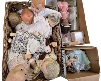 4131 - Wicker Basket & 2 Boxes Full of Dolls (Description): A wicker basket and two cardboard boxes  filled with an assortment of dolls. The  collection includes various vintage  composition and plastic baby dolls, cloth  dolls with yarn hair, and other character dolls in assorted sizes. Several dolls are  dressed in period clothing including floral  prints and lace-trimmed garments. The lot  features dolls in varying conditions,  representing different eras of doll making.