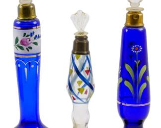 166 - 3 Vtg Hand Painted Glass Perfume Bottles (Description): Three vintage perfume bottles featuring hand  painted decorative designs. The collection  includes two cobalt blue glass bottles with  floral motifs and gold trim, each fitted with  clear glass stoppers and brass collars. The third bottle is clear glass