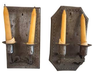 557 - 2 Metal Candleholders w/ Candles 10.5"x6" (Description): Two metal wall sconce candleholders with  candles included. The sconces feature punched  decorative borders along the edges and  ornate scrollwork brackets. Each holder  accommodates two taper candles. The metal displays an aged patina consistent with  vintage tinware. One sconce has a rectangular  backplate while the other features a  coffin-shaped design, both with keyhole  mounting slots. Measures 10.5" x 6".
