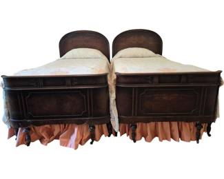 3702 - Pr Antique Mahogany Twin Beds w/ Bedding (Description): A pair of antique twin beds crafted in rich  mahogany with elegant curved headboards  featuring beautiful burl wood veneer panels.  The footboards display decorative inlay work  and paneled details with matching burl veneer centers. The beds rest on turned legs with  casters. Includes bedding consisting of  mattresses, floral patterned coverlets, and  pillows. Each bed measures 50 inches tall by  79 inches long by 42 inches wide.