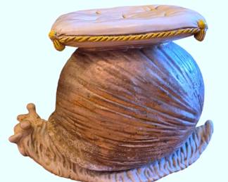 617 - Italian Snail Garden Stool 18"x24"x14" (Description): A whimsical ceramic garden stool in the form  of a large snail. The piece features a brown  glazed spiral shell with detailed texture and  a cream-colored body. The seat is fashioned  as a tufted cushion with gold rope trim and corner tassels.