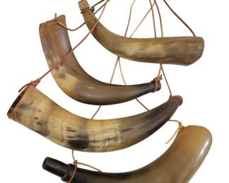 446 - Four Vintage Powder Horns (Description): A collection of four antique powder horns,  each featuring natural horn coloration with  characteristic mottled patterns in cream,  brown, and tan tones. The horns are fitted  with wooden plugs at the tips and have leather carrying straps attached. The horns  vary in size and curvature, displaying the  natural form of the original material. These  powder horns were traditionally used for  storing and dispensing black powder for