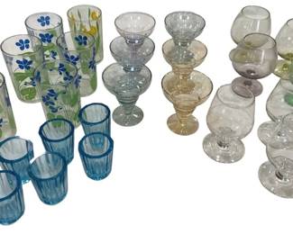 979 - Assorted Vintage Glasses (Description): The lot includes hand-painted floral juice  glasses with blue flower and green leaf  designs, tinted cocktail coupe glasses in  pale blue, amber, and purple hues, and  balloon-style wine glasses with colored bowls in green, pink, and clear variations.