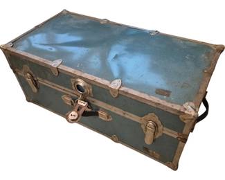 3946 - Vtg Blue Steamer Trunk Filled w/ Fabric (Description): Vintage blue steamer trunk filled with  fabric. The trunk features metal hardware  including corner protectors, latches, and a  central locking mechanism with padlock hasp.  The exterior shows a weathered blue finish with classic banding details. Measures 12  inches tall by 30 inches wide by 16 inches  deep.