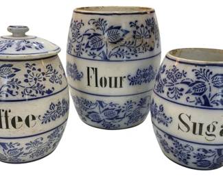 981 - Blue & White German Canister Set 82"x7" (Description): Featuring three ceramic canisters labeled  Coffee, Flour, and Sugar. Each piece is  decorated with traditional blue and white  floral and botanical motifs. The Coffee  canister retains its original lid with knob finial. The set shows characteristic  age-appropriate wear consistent with vintage  use. Measures 8.5"x7".