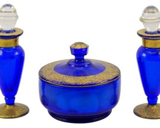 163 - 3pc Set Blue Perfume Set w/ Gold Overlay (Description): A set of three vintage blue glass perfume  pieces featuring two matching perfume bottles  with clear glass stoppers and one covered  powder jar. The pieces are decorated with  gold embellished accents at the rims, bases, and lid.