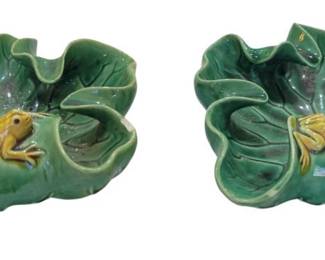 681 - 2 Majolica Frog Adorned Ashtrays (Description): A pair of frog ashtrays featuring decorative  frog motifs. These pieces are designed in the  form of lily pads with frogs perched on the  edge, finished in green glaze with  yellow-toned frogs.