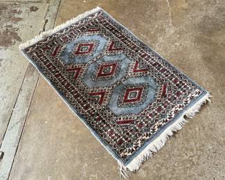This lot features a small, hand-knotted Persian rug featuring a traditional Kazak geometric pattern with red diamond motifs on a light blue field that measures, 36” H x 24” W.