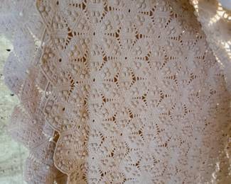 This lot features a vintage hand-crocheted lace bedspread with an intricate circular motif design and cream color. This piece is in excellent condition and comes with an additional piece for the pattern.