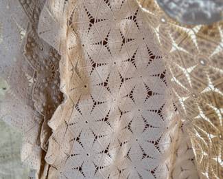This lot features a vintage hand-crocheted lace bedspread with an intricate circular motif design and cream color. This piece is in excellent condition and comes with an additional piece for the pattern.