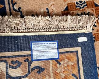 This lot features a Karastan Cathay Medallion area rug featuring a beige field and blue borders that measures, 120” H x 104” W.
