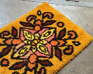 This lot features a latch hook tapestry created in the "rya style, " a shaggy textile technique that became a home decor staple in the 1960s and ’70s. This piece measures, 28” H x 20” W.