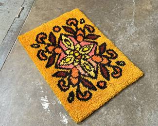 This lot features a latch hook tapestry created in the "rya style, " a shaggy textile technique that became a home decor staple in the 1960s and ’70s. This piece measures, 28” H x 20” W.