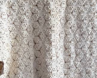 This lot features a vintage hand-crocheted lace bedspread with an intricate circular motif design and cream color. This piece is in excellent condition and comes with an additional piece for the pattern.