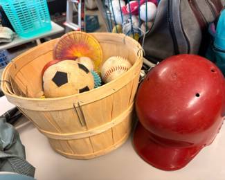 Bushel basket of sports balls and red batting helmet
