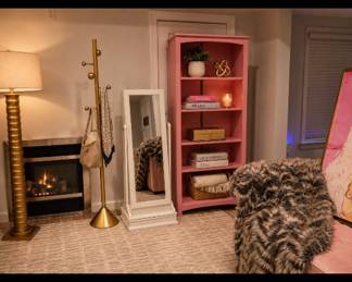 Pink bookshelf, gold floor lamp, floor mirror, faux fur throw blanket, contemporary abstract art, feminine decor, modern glam furnishings, accent lighting, designer-inspired styling, curated home decor